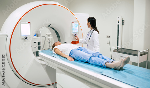 Professional Doctor Radiologist In Medical Laboratory Controls magnetic resonance imaging or computed tomography or PET Scan with Female Patient Undergoing Procedure.