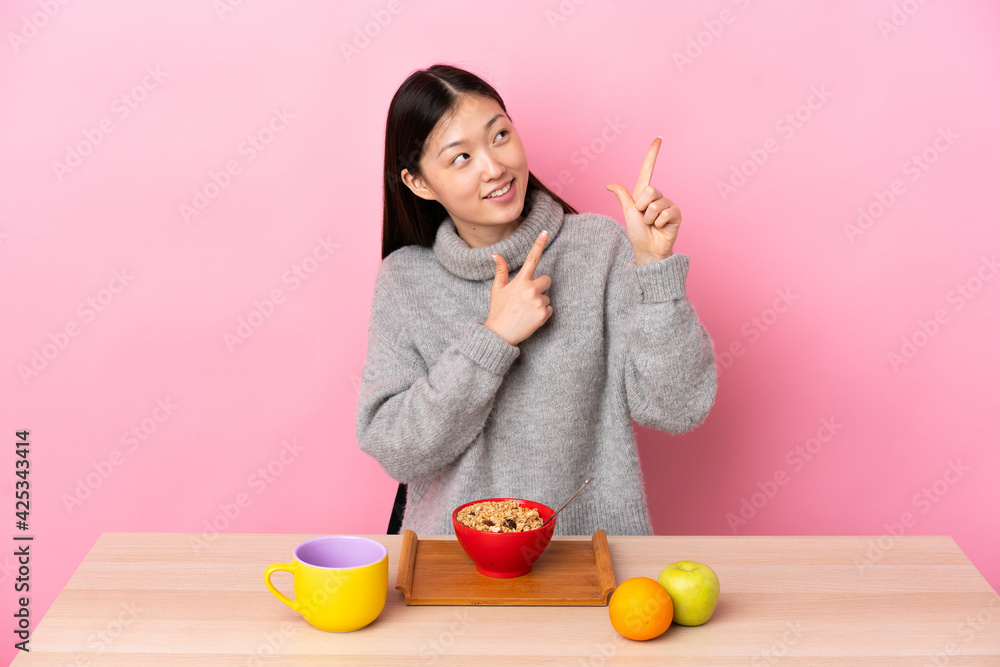 Young Chinese girl having breakfast in a table pointing with the index ...