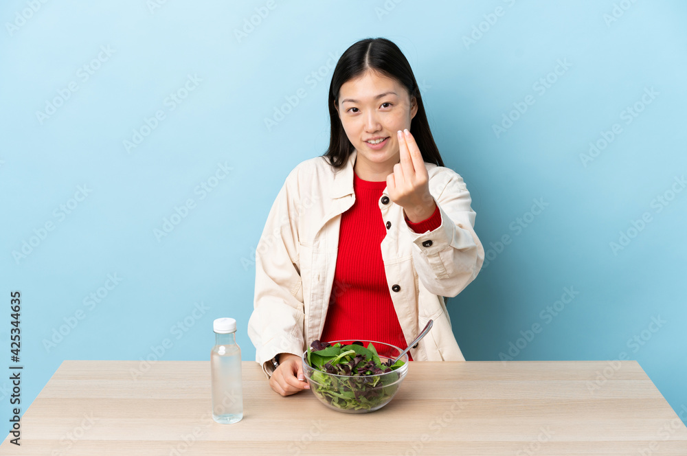 Young Chinese girl eating a salad making money gesture Young Chinese girl eating a salad making money gesture