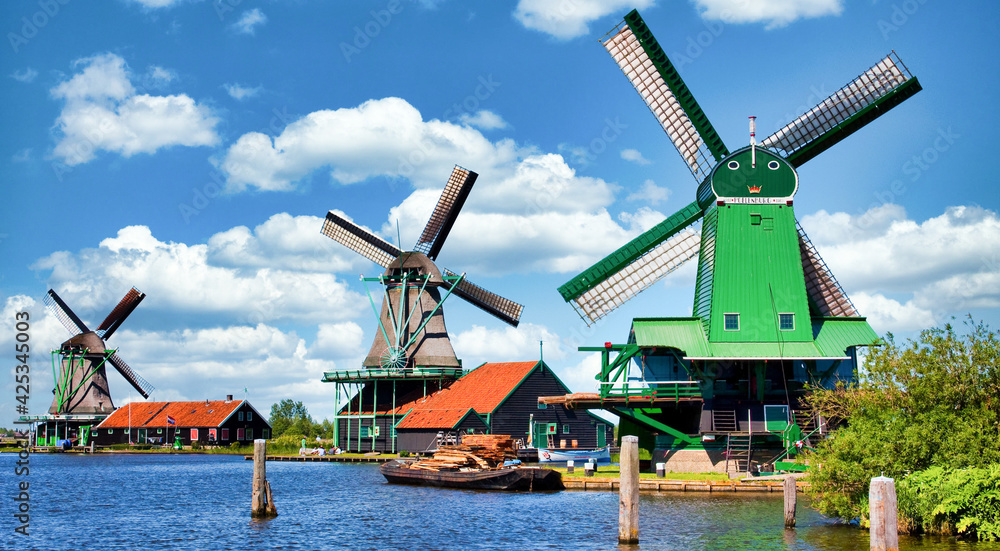 Dutch windmill in green countryside close to Amsterdam, Netherlands, with blue sky and river water.