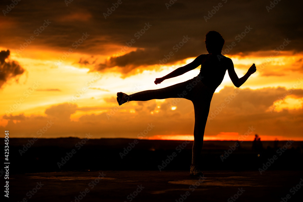 Silhouette of a fitness woman stretching at sunset with the sun in the background
