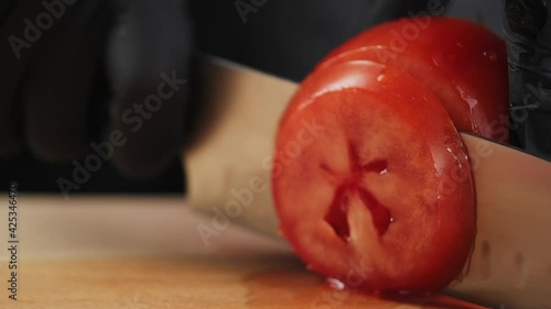 Close-up of a chef cutting a red tomato with a knife on a wooden board. Slicing a tomato with a knife. Cutting vegetables