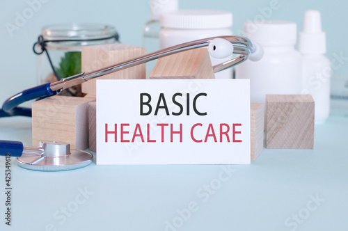 BASIC HEALTH CARE - text on card on wooden table with stethoscope, medical pills and wooden blocks