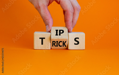 Tips and tricks symbol. Businessman turn the wooden cube and changes the word 'tips' on 'tricks'. Beautiful orange background. Business and tips and tricks concept, copy space. photo