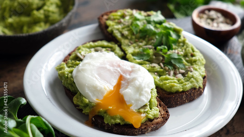 Toast with mashed avocado and poached egg. Rye bread avocado toast with runny egg yolk poached egg cut and mixed seeds