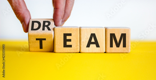 Dream team symbol. Businessman turns the cube and changes the word 'dream' to 'team'. Beautiful yellow table, white background. Business and dream team concept, copy space.