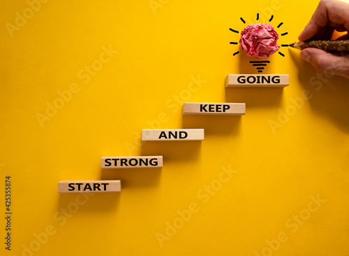 Start strong and keep going symbol. Concept words 'Start strong and keep going' on wooden blocks on a beautiful yellow background. Businessman hand. Business, motivational and start strong concept.