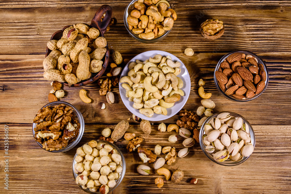 Various nuts (almond, cashew, hazelnut, pistachio, walnut) in bowls on a wooden table. Vegetarian meal. Healthy eating concept. Top view Various nuts (almond, cashew, hazelnut, pistachio, walnut) in bowls on a wooden table. Vegetarian meal. Healthy eating concept. Top view
