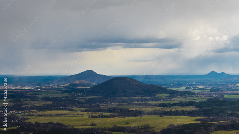 scenic view of Mount Ralsko and Mount Tlustek in the Bohemian Lusatian Mountains as seen from Mount Hochwald in Germany with storm clouds and rain plumes