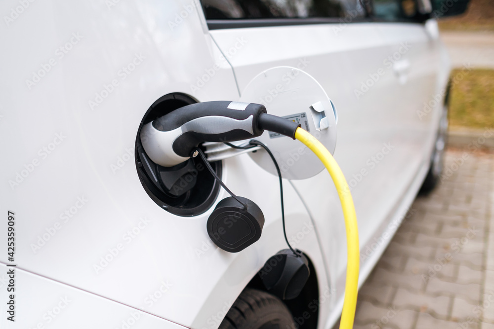 A white electric car charging at the charging station in the street. A white electric car charging at the charging station in the street.