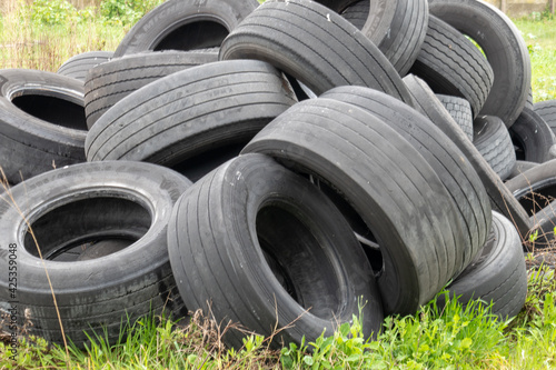 Pile of old rubber tyres in a green field. Stack abandoned car wheels