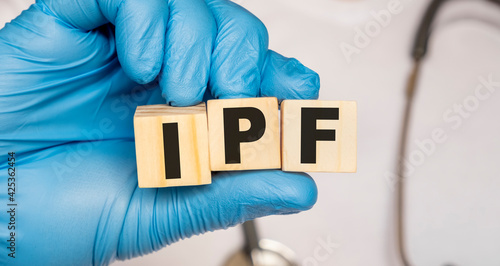 IPF Idiopathic pulmonary fibrosis - word from wooden blocks with letters holding by a doctor's hands in medical protective gloves. Medical concept. photo