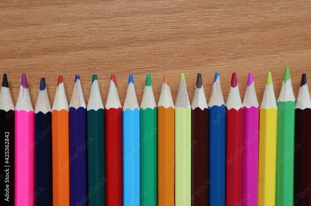Colored pencils laid out in a row on a brown surface. Colored pencils laid out in a row on a brown surface.