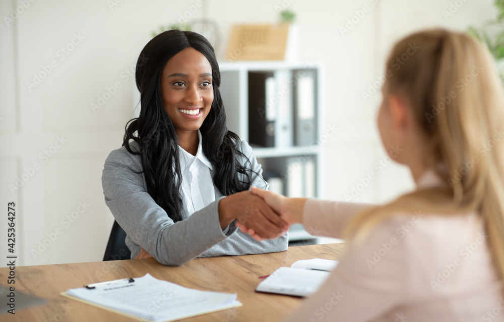 Unrecognizable black HR manager shaking hands with female job appicant on employment interview at office Unrecognizable black HR manager shaking hands with female job appicant on employment interview at office