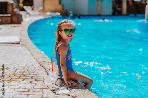 Young pretty girl in blue bikini and sun glasses sitting near the pool with cocktail and smiling. Copy space.