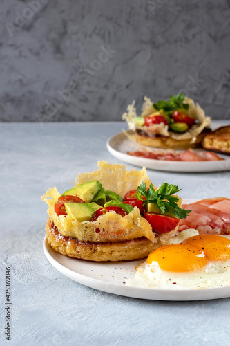 Crumpets are traditional in English-speaking countries lush pancakes made from yeast dough with cheese, avocado and cherry tomatoes. With eggs and fried bacon for breakfast. Selective focus.