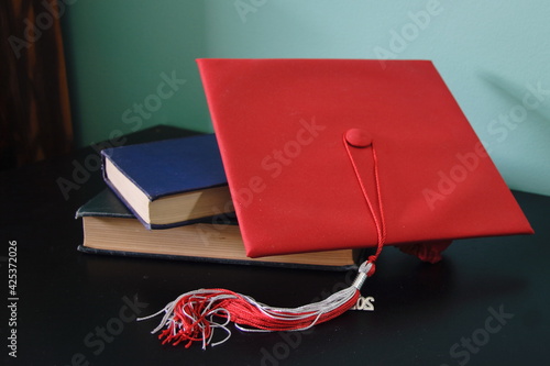 Red graduation cap laying diagonally across books