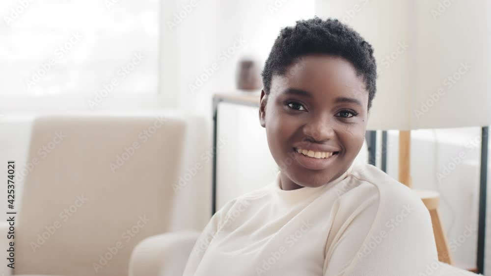 Portrait afro american girl ethnic model with short hair looking to side sitting in profile at home turns head looks at camera smiling toothy, close-up happy african mixed race woman posing indoors Portrait afro american girl ethnic model with short hair looking to side sitting in profile at home turns head looks at camera smiling toothy, close-up happy african mixed race woman posing indoors