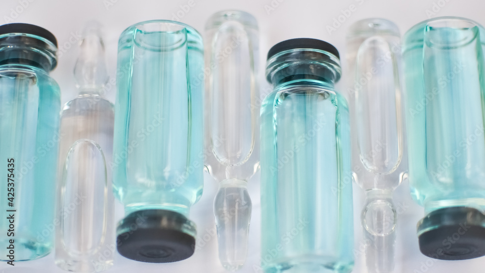 Vial vaccine, top view of glass ampoules with transparent and blue liquid lying on white background, global vaccination concept Vial vaccine, top view of glass ampoules with transparent and blue liquid lying on white background, global vaccination concept