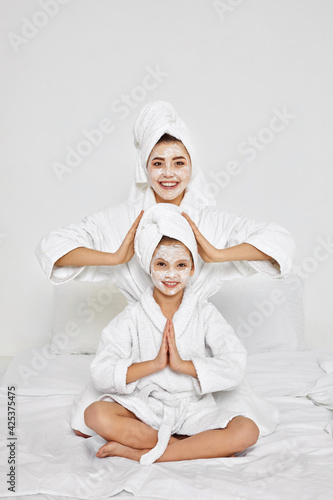 mother and daughter are sitting with towels on head and facial mask.