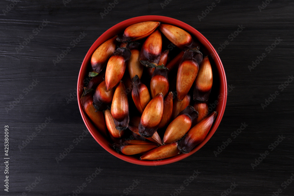 Typical araucaria seeds used as a condiment in Brazilian cuisine in winter. Brazilian pinion nuts in brown and red wooden bowl on gray wooden background Typical araucaria seeds used as a condiment in Brazilian cuisine in winter. Brazilian pinion nuts in brown and red wooden bowl on gray wooden background