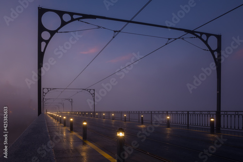 City street, a bridge with tram tracks. The foggy morning before dawn. Blue sky with pink clouds. Rows of low lanterns along the edges of the road. Linear perspective.