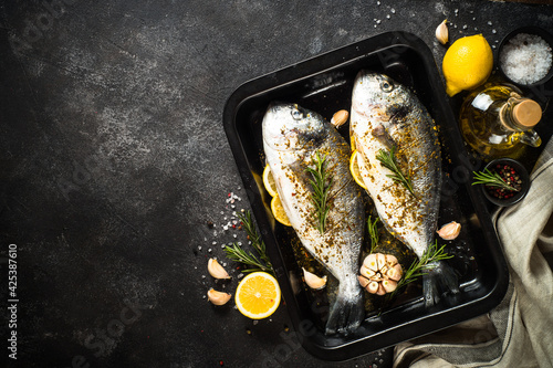 Canvas Print Raw fish dorado in baking sheet at black stone table.