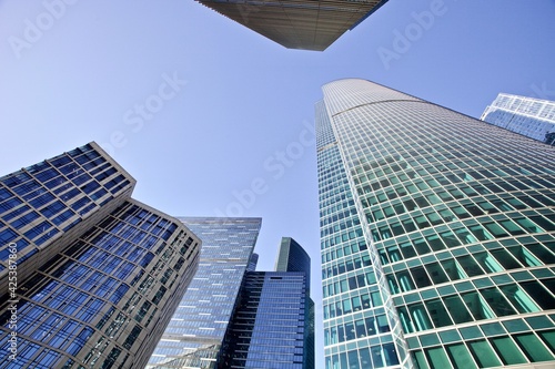 Modern office buildings against bright blue sky. Bottom-up view. Glass facades of tall skyscrapers with bright sun glare and reflections. Economy development, finance and business concept. Downtown.
