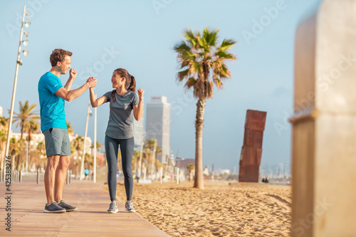 Friends teamwork interracial athletes couple happy of strong success in reaching goal training together. Runners working out outside on beach outdoor gym.