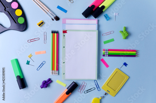Notebooks, pencils, markers and other stationery lie on a blue background. Concept back to school, goods for school, office, flat layout, space copying, selective focus