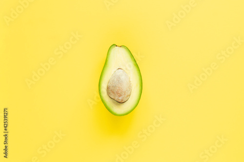 A half of avocado with seed on yellow background. Top view.