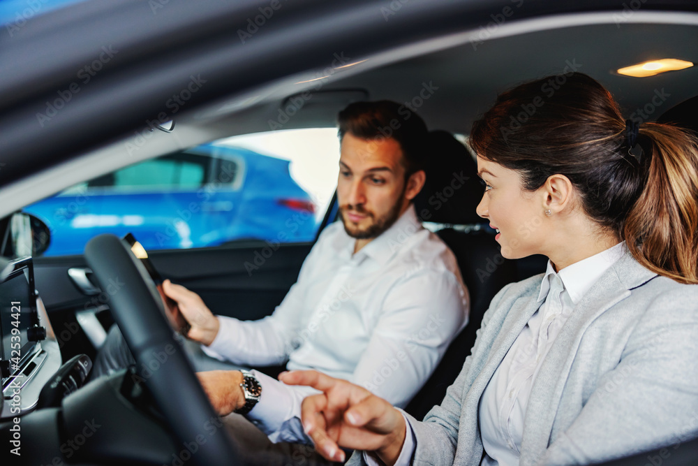 Car seller sitting in a car with a customer and showing him advantages and performances of a car. Car seller sitting in a car with a customer and showing him advantages and performances of a car.
