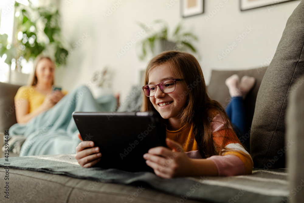 Young girl is using tablet computer while mom is in the background. Living room. Young girl is using tablet computer while mom is in the background. Living room.