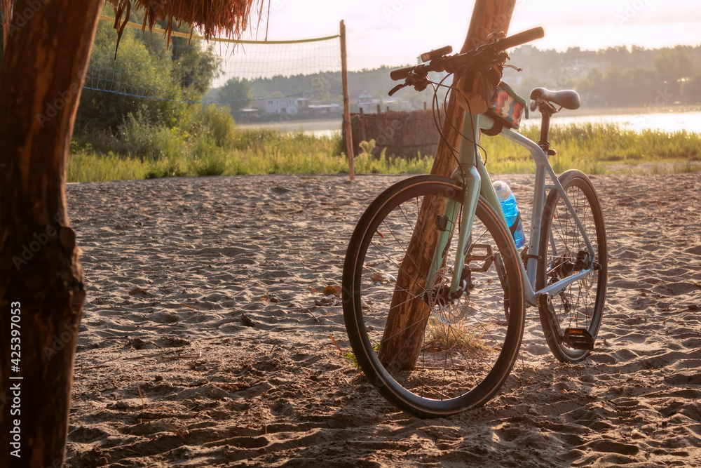Naklejka premium Road bike on a sandy beach by the river at sunrise.