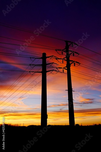 A silhouette of overhead power lines at sunset used in electric power transmission and distribution to transmit electrical energy across large distances suspended by towers or poles