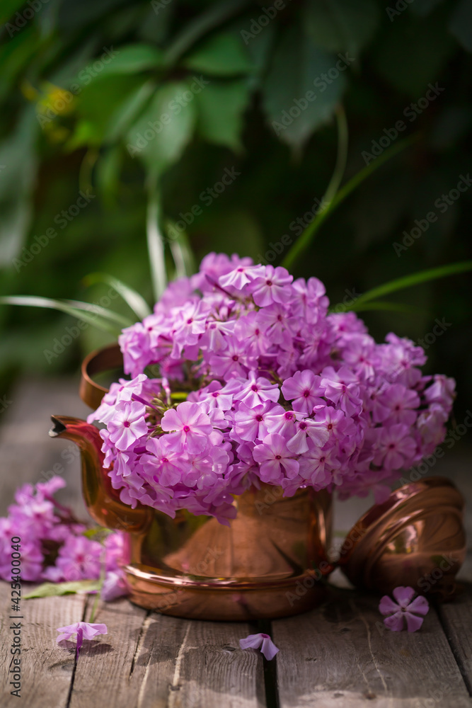 Pink phloxes in a copper teapot on a wooden table in the garden. Summer bouquet Pink phloxes in a copper teapot on a wooden table in the garden. Summer bouquet