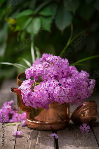 Pink phloxes in a copper teapot on a wooden table in the garden. Summer bouquet