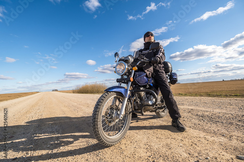  man in a black uniform on bike against the backdrop of panorama of field and blue sky. motorcycle travel concept