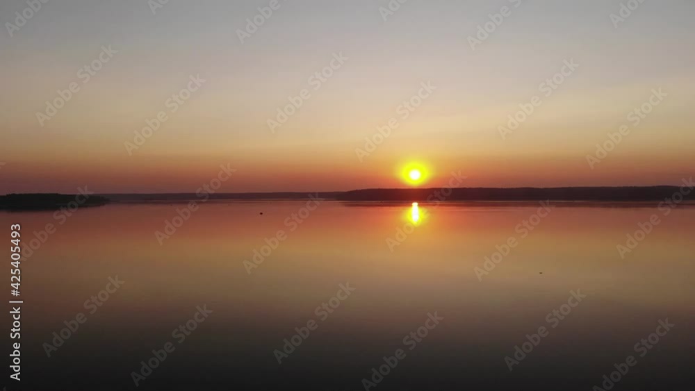Shooting from a drone of a summer sunset over a lake surrounded by forests and an orange path from the sun on the water Shooting from a drone of a summer sunset over a lake surrounded by forests and an orange path from the sun on the water