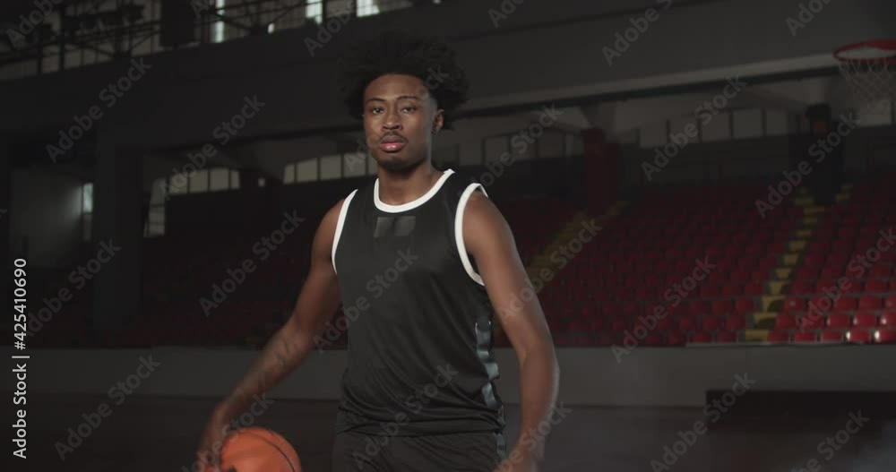 Video portrait of a basketball player bouncing a ball. African american man in uniform posing inside sports hall Video portrait of a basketball player bouncing a ball. African american man in uniform posing inside sports hall