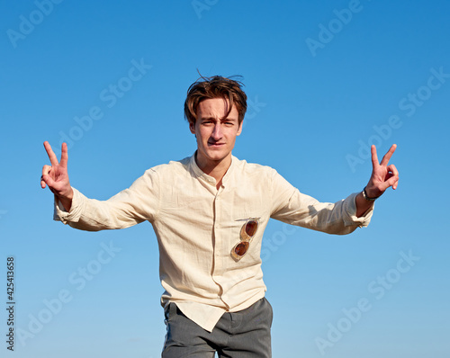 A Caucasian man from Spain making peace signs with both hands on clear sky background