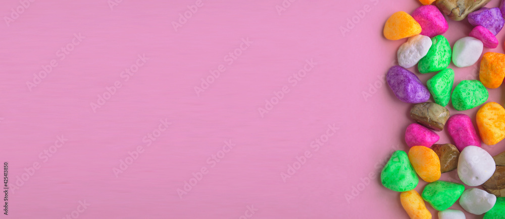 Obraz premium Colored stones, on a pink background, top view, lying on a flat surface, banner