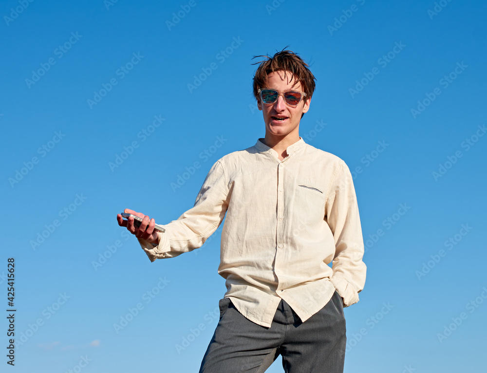 A Caucasian man holding his phone and talking with one hand in pocket on sky background A Caucasian man holding his phone and talking with one hand in pocket on sky background