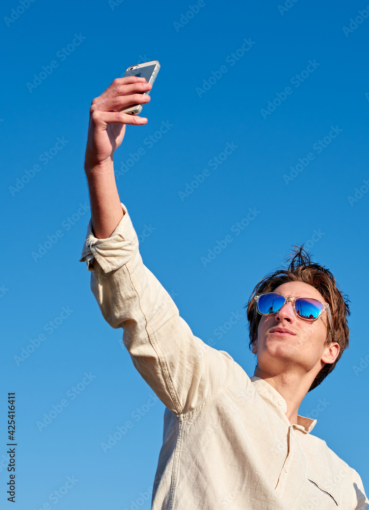 Spanish white man with long hair, purple glasses and a beige shirt taking a high angle selfie on clear blue sky background Spanish white man with long hair, purple glasses and a beige shirt taking a high angle selfie on clear blue sky background