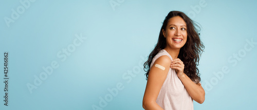 Foto Woman Showing Vaccinated Arm With Bandage After Injection, Blue Background
