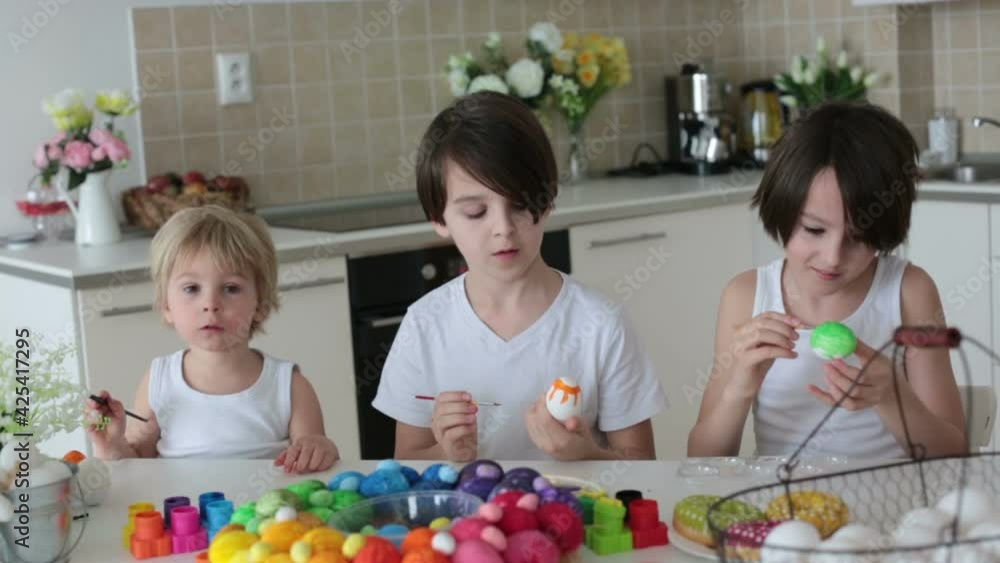 Three children, sibling brothers, painting easter eggs for decoration at home, mother helping them Three children, sibling brothers, painting easter eggs for decoration at home, mother helping them