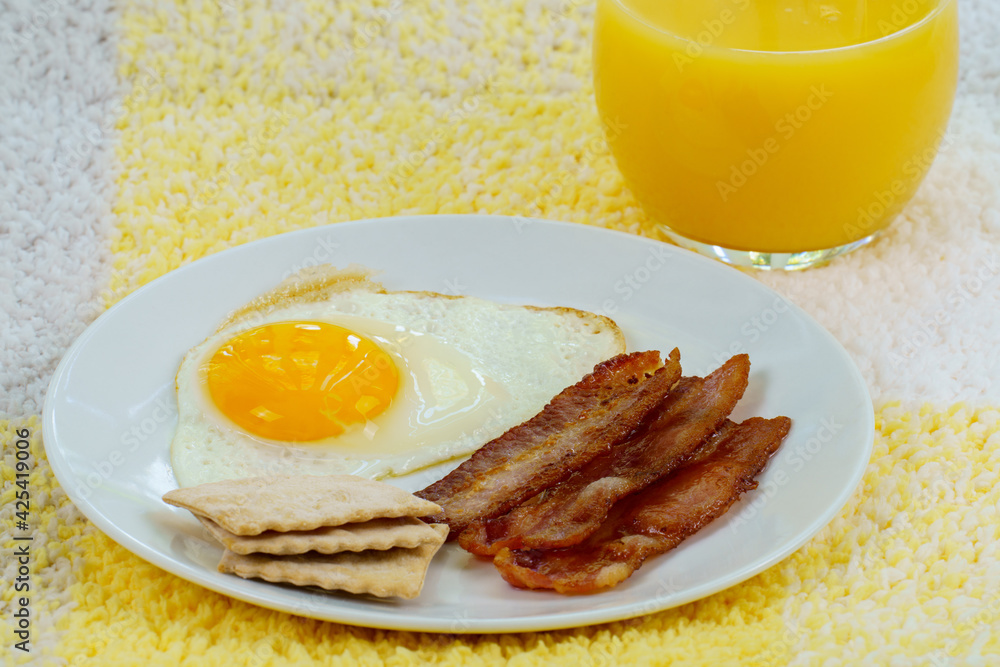 Fototapeta premium Fried fresh egg and bacon on white plate and orange juice