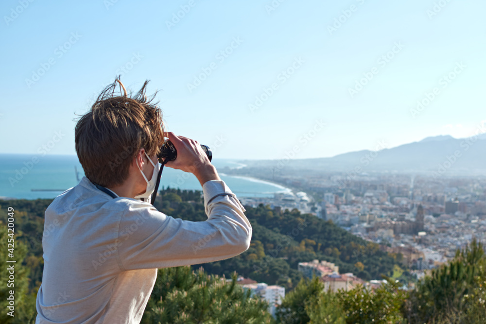 A close up of a young man from Spain in a white shirt wearing a mask observing the city of Málaga through binoculars A close up of a young man from Spain in a white shirt wearing a mask observing the city of Málaga through binoculars