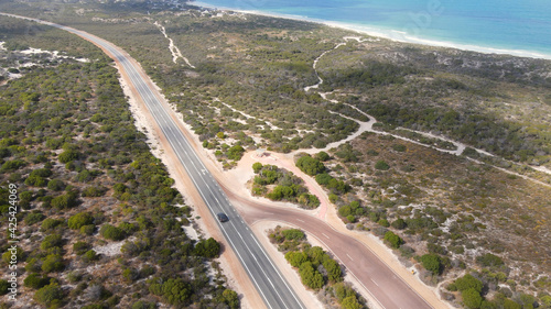 Aerial shot of one car driving through nice and clean Australian rural Road front to ocean during sunny day
