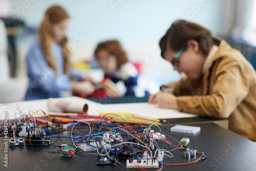 Group of children building robots in engineering class at school, focus on wires and electric circuits in foreground, copy space
